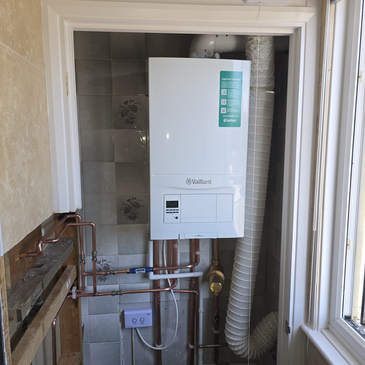 Boiler installation in a tiled utility cupboard with ventilation ducting and flue
