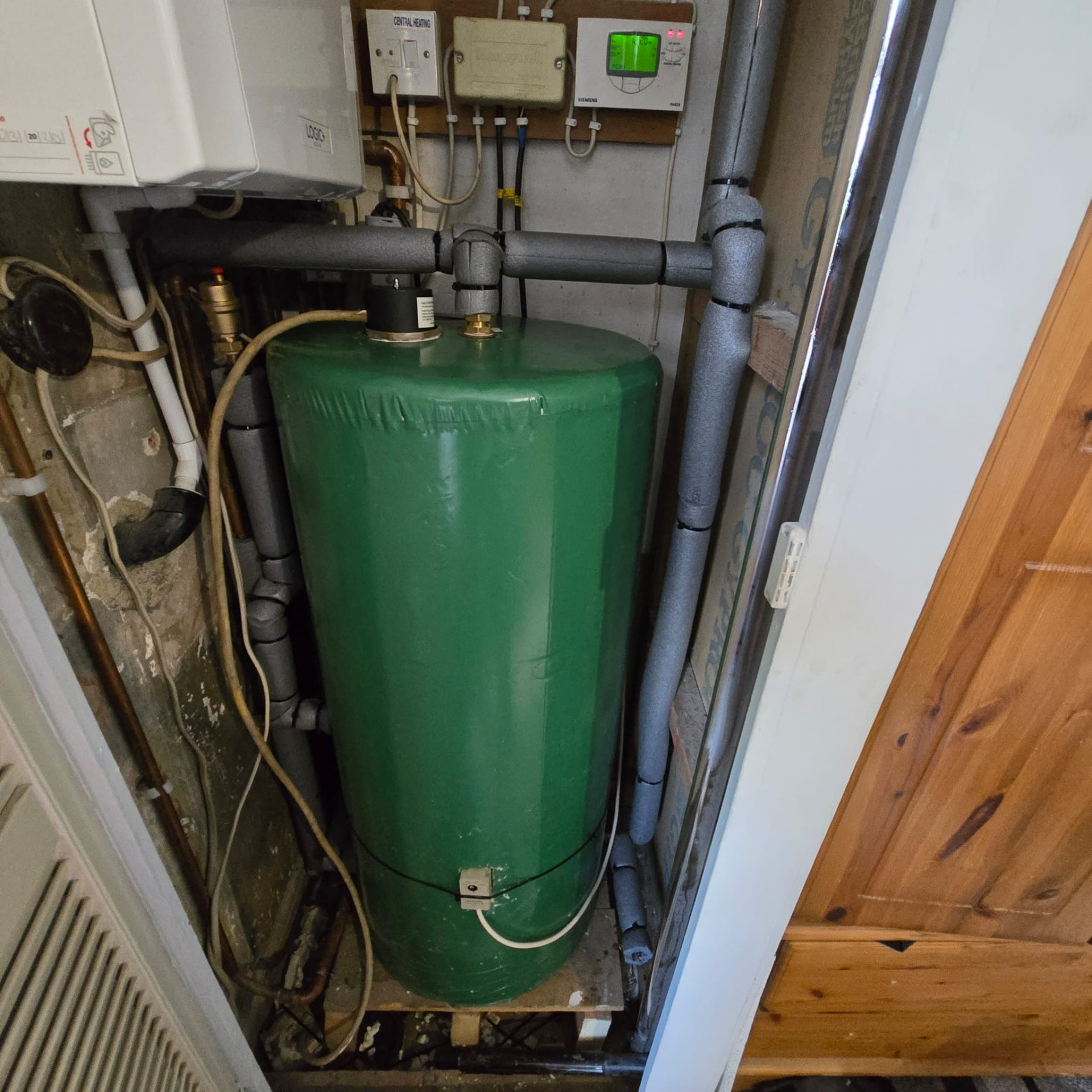 Old hot water cylinder with untidy pipework before replacement in an airing cupboard