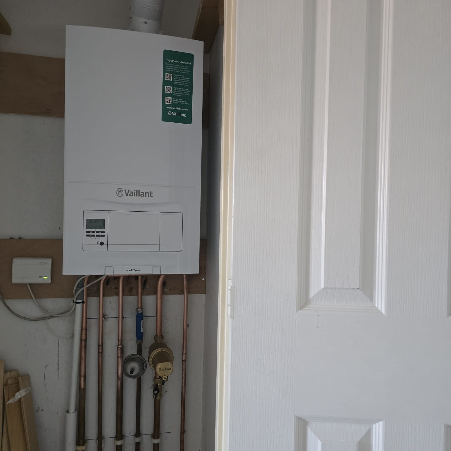 Close-up of copper pipework and isolation valves under a cupboard-mounted Vaillant boiler