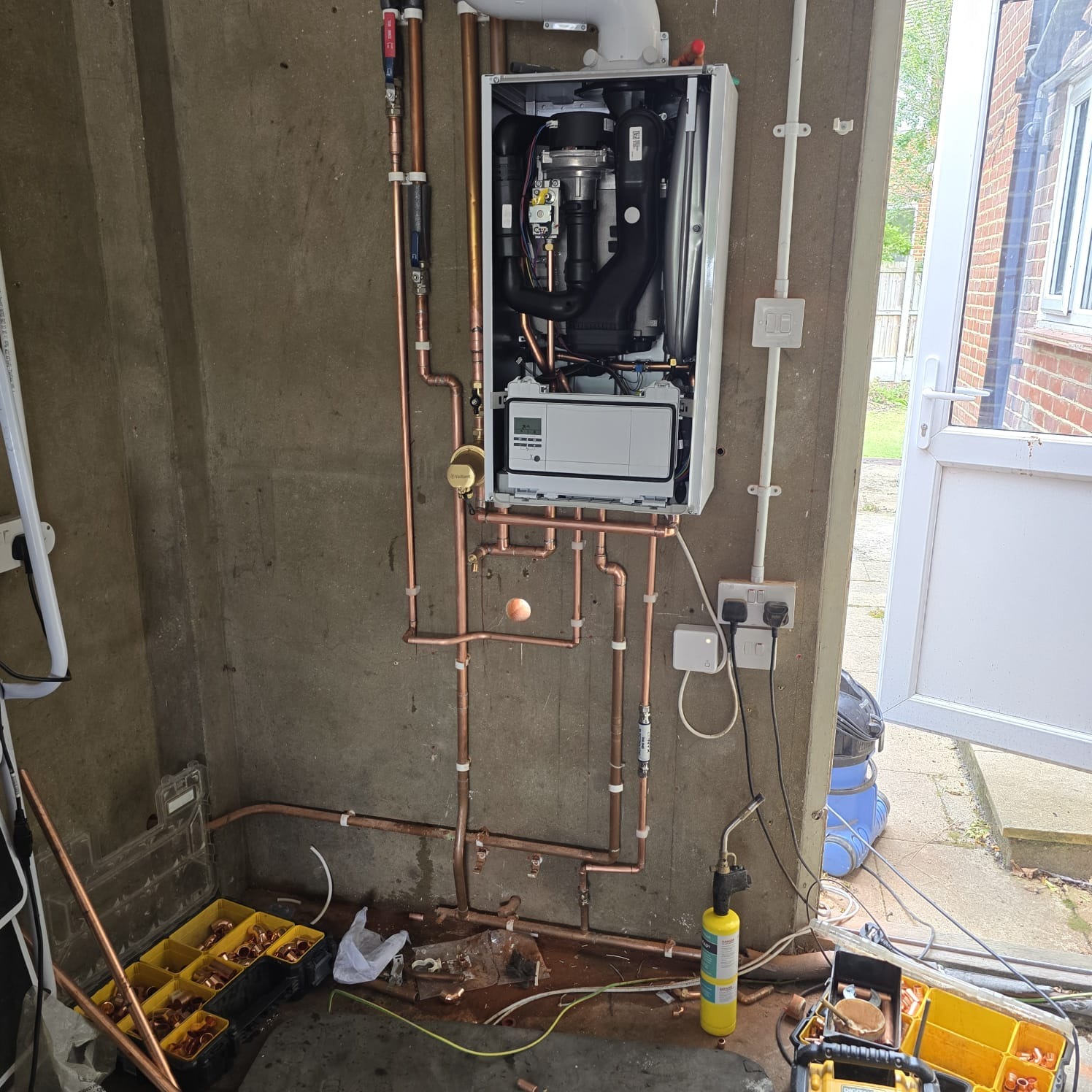 Open Vaillant boiler during installation showing new copper pipework on a concrete wall