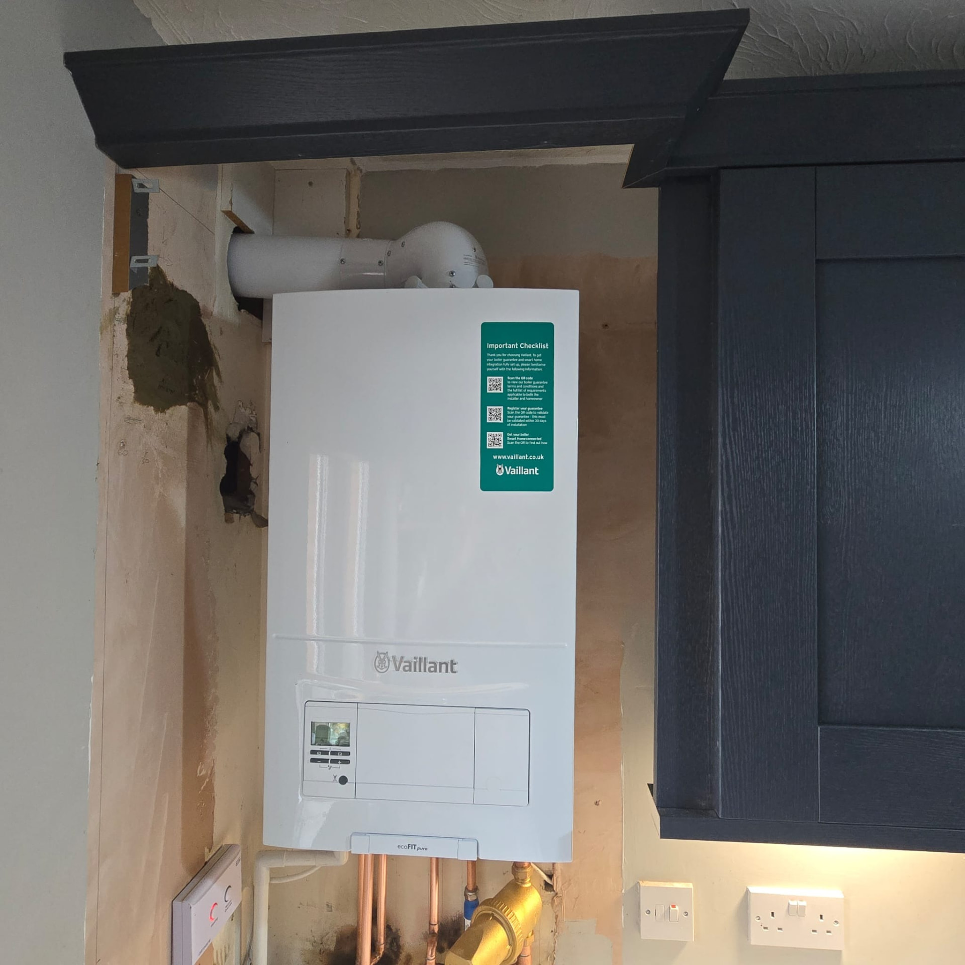 Combi boiler installed between a grey kitchen unit and wall with tidy copper pipework